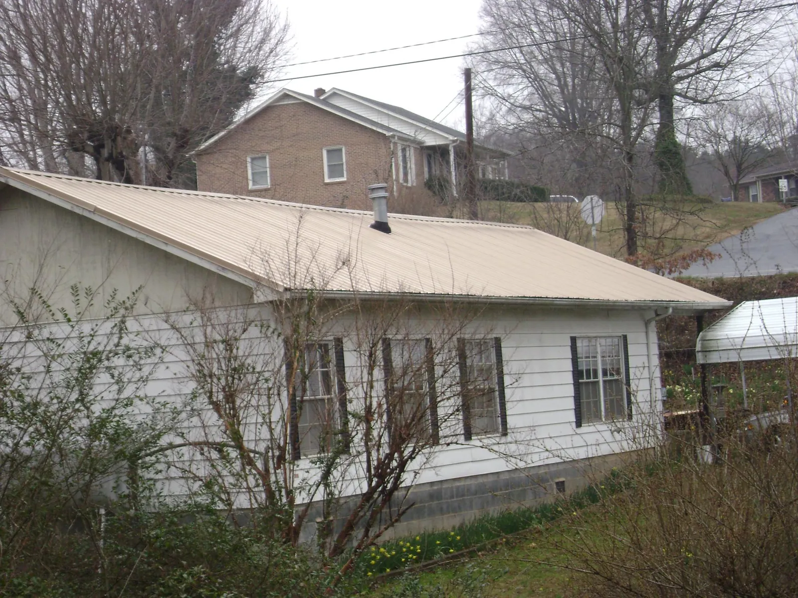 Tan metal roof on a white sided house set into a hillside — Commercial Roofing by Roofing Brothers in Dresden